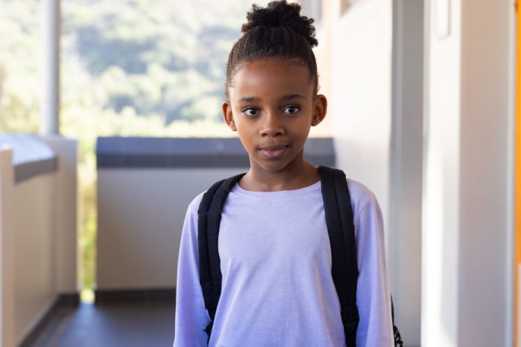 In school, african american girl with backpack standing in hallway, looking at camera. Education, student, youth, learning, childhood, campus